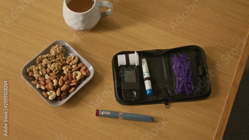 Top view of diabetes testing kit, insulin pen, and bowl of healthy nuts sitting on wooden table. Footage ideal for healthcare campaigns, diabetes awareness, and medical marketing
