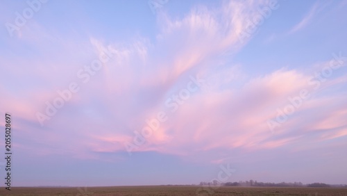 Sunset sky with pink and blue clouds, over a rural landscape at twilight.
