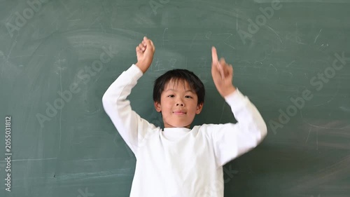 黒板の前で両手で上を指差して案内する男子小学生