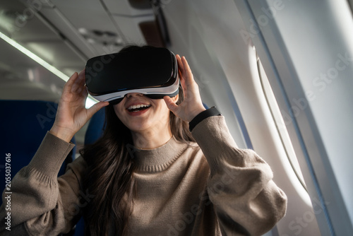 Young woman using a virtual reality headset while sitting by the window on an airplane, enjoying immersive entertainment during a flight with a modern travel lifestyle feel.