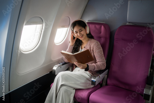Young woman relaxing in an airplane seat, wearing headphones and reading a book by the window during a calm flight