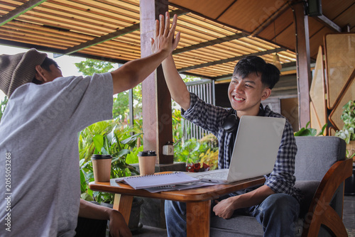 Two Asian Men Sit At Wooden Table In An Outdoor Cafe