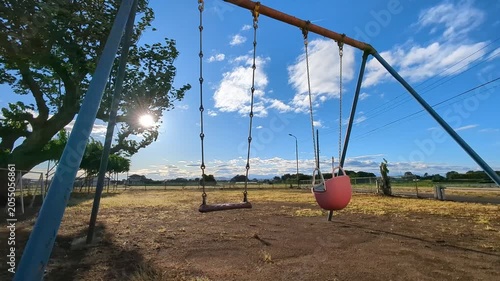 4K slow‑motion shot of an empty swing swaying in the wind at a rural park with backlit sunlight through tree branches