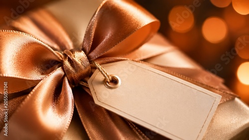Golden gift box with blank tag and elegant ribbon bow for celebration.