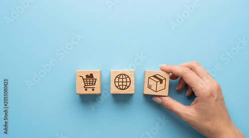 Hand picking wooden block with package icon near shopping cart and globe