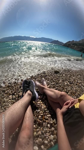 family of three relaxing on a pebble beach by blue sea