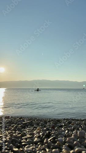 Calm sea sunset with rocky shore and swimmer