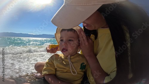 Toddler on a sunny beach with adult help use sun cream protection