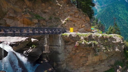 Slow motion shot of water stream with a metal bridge above it in the Himalayan mountain valley near Manali in Himachal Pradesh, India. Scenic view of a bridge in rural area of the Himalayas.