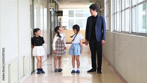 学校の廊下に並んで笑顔で立つ男性教師と女子小学生たち