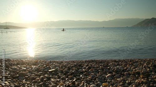 Calm sea sunset with rocky shore and swimmer