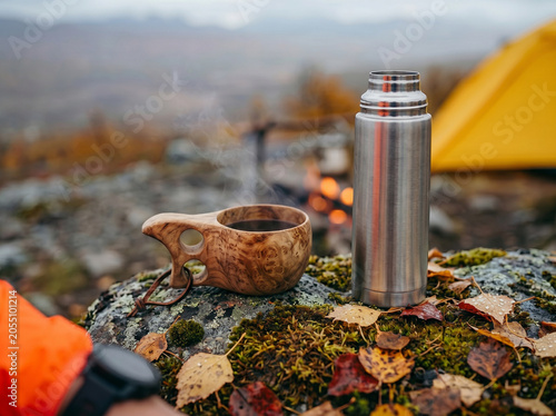 Wooden kuksa cup and thermos by campfire in Nordic Lapland like autumn nature