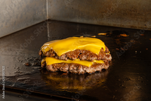 Close up of two juicy beef burger patties stacked with melted cheddar cheese on a hot flat top griddle