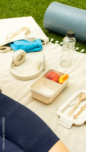 Woman relaxing on a picnic blanket with healthy snacks and exercise gear