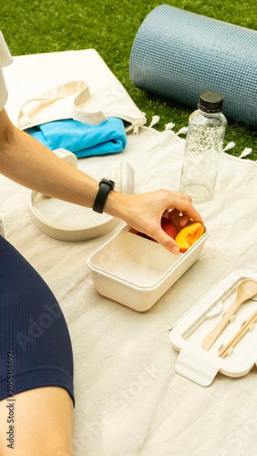 Woman preparing a healthy snack outdoors with a yoga mat and water bottle