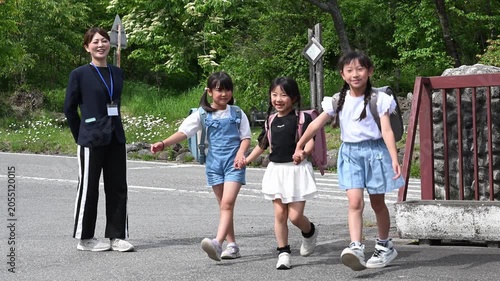 学校の校門で先生に見守られ手をつないで登校する女子小学生たち