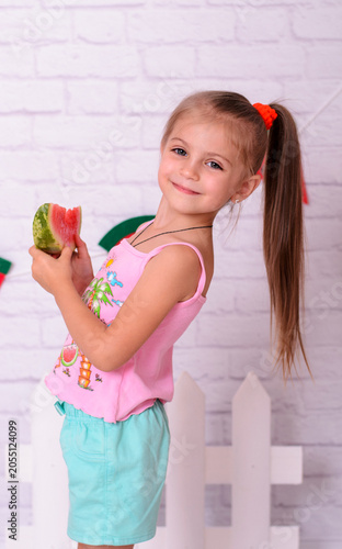 Cheerful child with a long ponytail holding a piece of watermelon, smiling at the camera.
