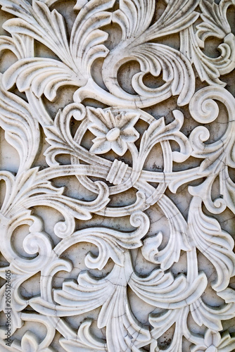Close up of an intricate white marble relief featuring floral motifs and scrolling ornamental patterns. Architectural detail showcasing craftsmanship and decorative design.