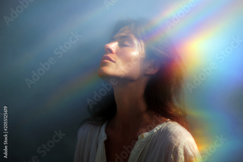 Woman inhaling light with soft rainbow rays across her face for spiritual healing background and wellness design