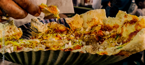 Foto A hand breaking a piece of crispy masala papad chaat topped with sev, chopped on