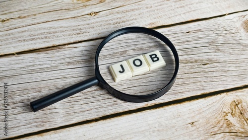 Foto A black magnifying glass focuses on the word JOB spelled out with white tiles on a light wooden background, symbolizing career exploration, employment hunting, and recruitment concepts