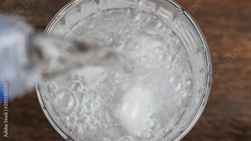 Pouring sparkling water from bottle in glass with ice cubes, close up