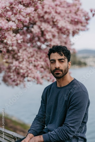 Seated man portrait beside pink magnolia tree at lakeside in spring for portrait background and editorial banner design