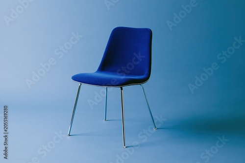Comfortable upholstered armchair with sleek metal legs on a minimalist blue background