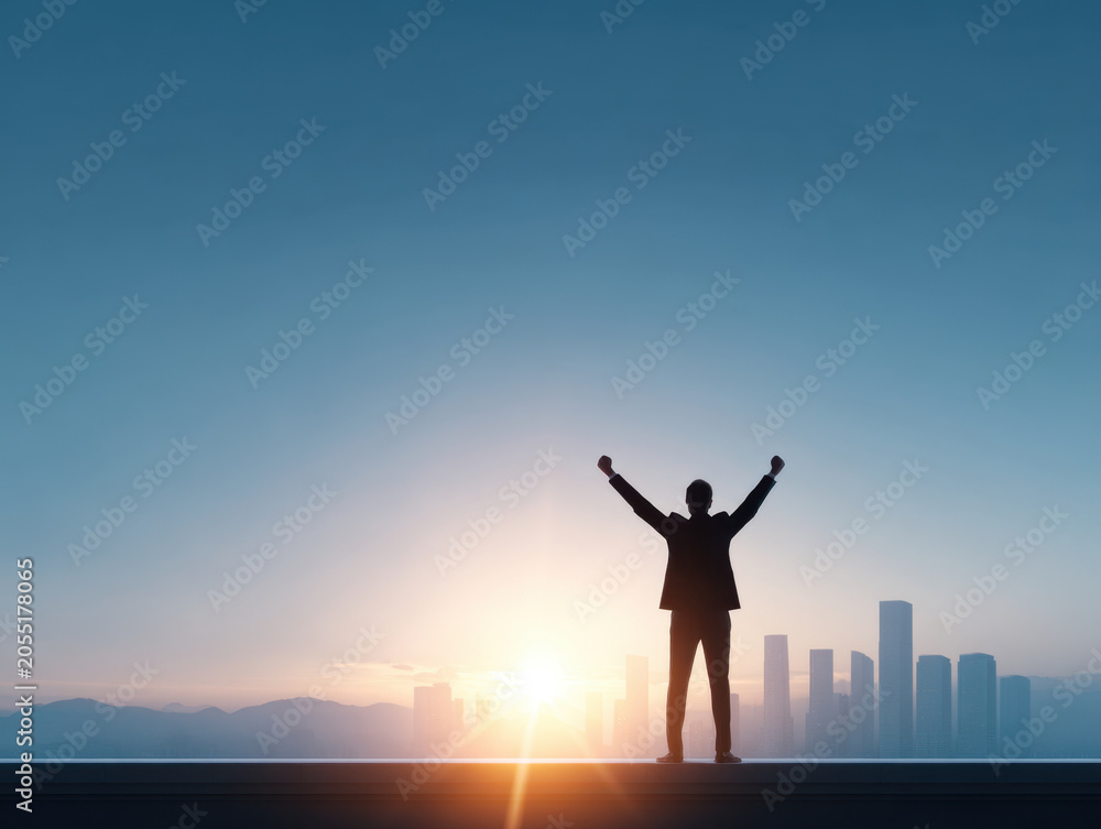 Fototapeta premium Silhouette of businessman with arms raised at sunrise over city skyline, success and victory concept