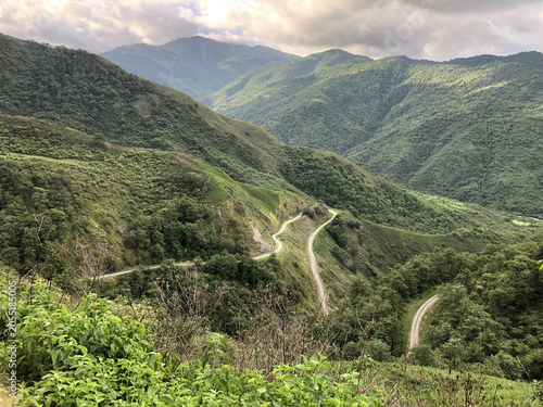 Winding mountain road crossing lush green valleys in the Andes. Scenic landscape with rolling hills, dense vegetation and dramatic terrain, showcasing the beauty of a remote highland region.