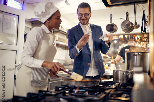 Cook in Professional Modern  kitchen, restaurant concept. Smiling manager looking at orders with female chef in kitchen.
