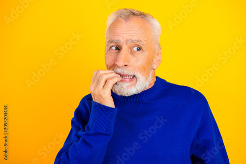 Φωτογραφία Senior man biting his nails and looking worried against a bright yellow backgrou