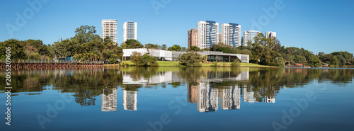 Fényképezés Panoramic view of Lake Igapó in the city of Londrina, highlighting modern buildings reflected in the calm waters under a clear sky