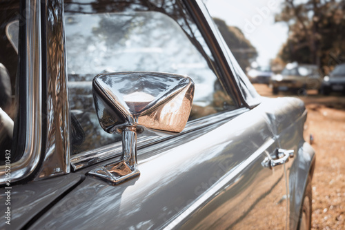 Chrome side mirror mounted on a classic car door, featuring a polished metallic finish and reflections of the surroundings.