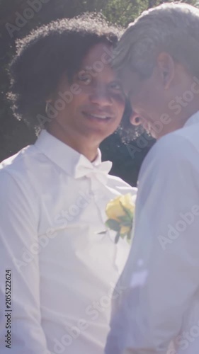 Vertical video: Leaning couple sharing forehead touch in garden, loving, white shirts, yellow rose