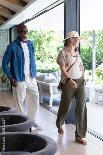 Diverse couple walking toward patio through open glass wall, woman wearing straw hat, copy space