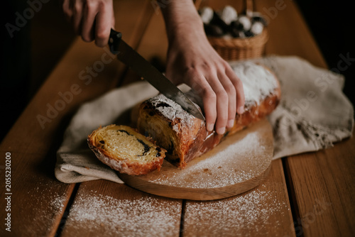 Close-up of baker hands slicing a fresh homemade sweet pastry roll with a knife on a wooden board, rustic food styling.