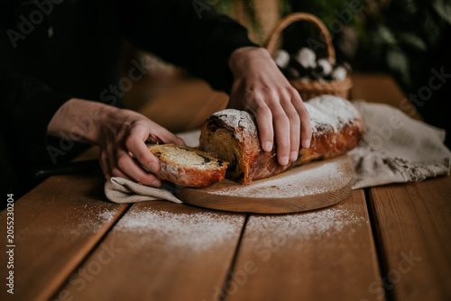 Close-up of baker hands slicing a fresh homemade sweet pastry roll with a knife on a wooden board, rustic food styling.