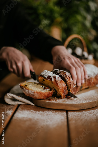 Close-up of baker hands slicing a fresh homemade sweet pastry roll with a knife on a wooden board, rustic food styling.