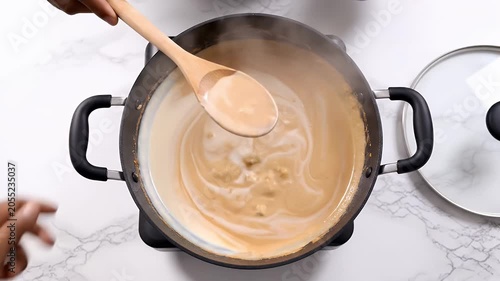 Creamy Sauce Being Stirred in a Cast Iron Pot by Two Hands in Kitchen
