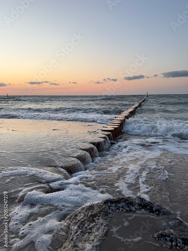Sunset at the Baltic Sea with waves washing around a wooden groyne