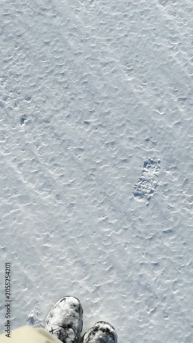 First-person view walking across frozen snow and icy ground in a winter landscape. Camera rises to reveal a vast frozen wilderness, capturing adventure, exploration and cold weather. Vertical Video