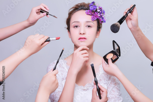 Fotografie Elegant young woman receiving bridal makeup with flowers in hair