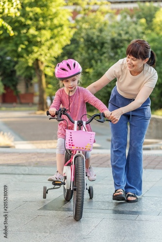 Mother Teaching Child to Ride Bicycle with Safety Helmet
