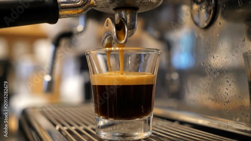 Coffee pours from espresso machine into glass cup