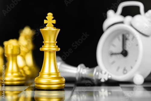 Φωτογραφία Golden chess king with alarm clock and defeated rival representing leadership and time pressure