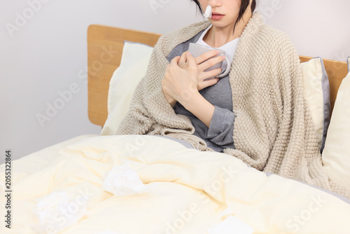 Valokuva Sick young woman in bed with blanket and hot drink recovering at home