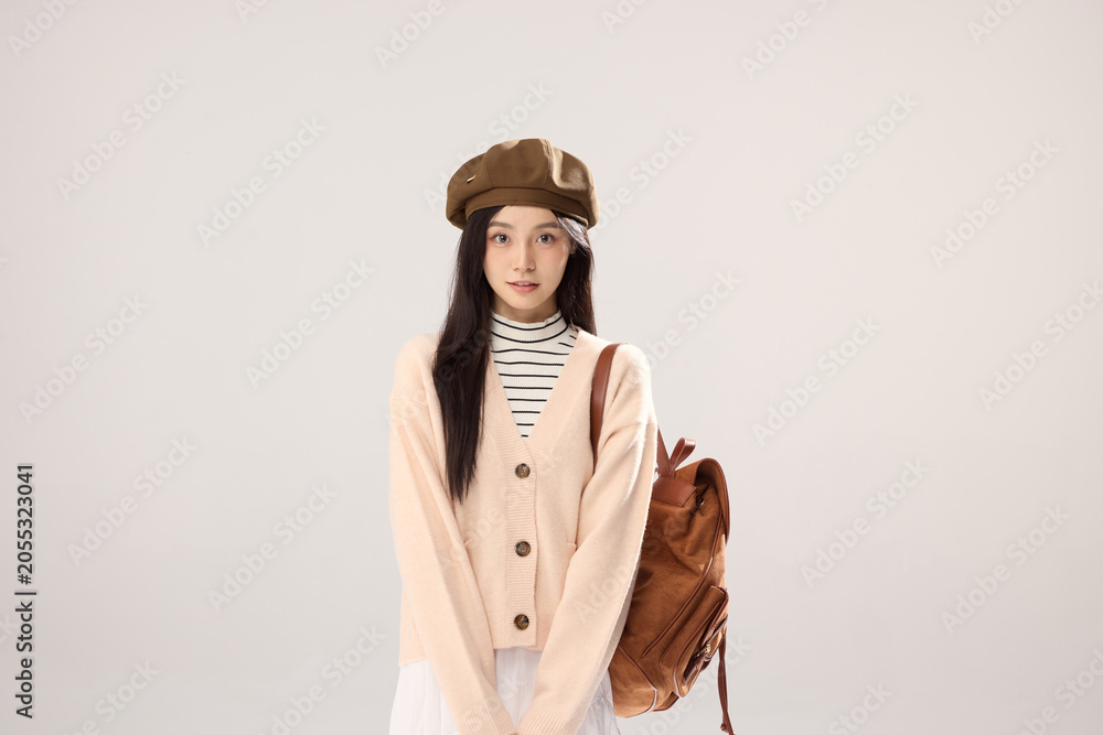 Fototapeta premium Stylish young woman in beret with backpack on neutral studio background