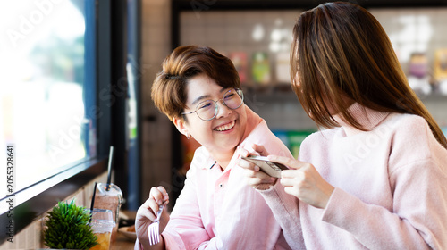 Portrait Asian positive young bearded and beautiful attractive LGBTQIA women barista couple smile and enjoy working together at the modern coffee shop. Digital marketing and Coffee Business Concept.