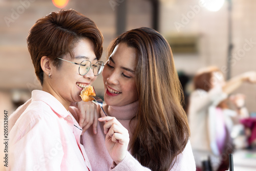 Portrait Asian positive young bearded and beautiful attractive LGBTQIA women barista couple smile and enjoy working together at the modern coffee shop. Digital marketing and Coffee Business Concept.